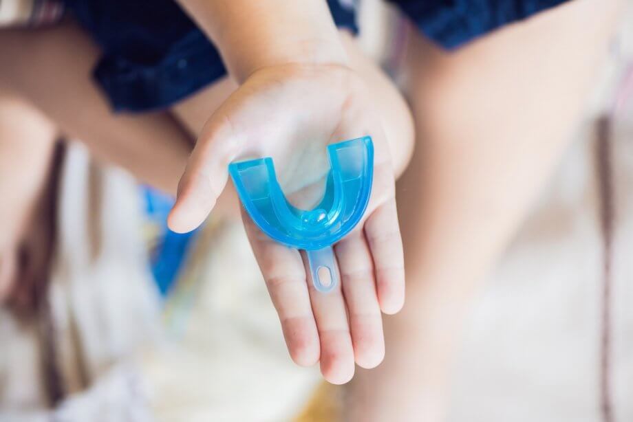 Photograph of a persons hand holding a blue mouthguard.